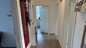 A narrow hallway with a wooden floor, a white door at the end, and a coat rack on the left. - Haus am Röblinsee - Stork vacation apartment in Fürstenberg / Havel (Fürstenberg/Havel)