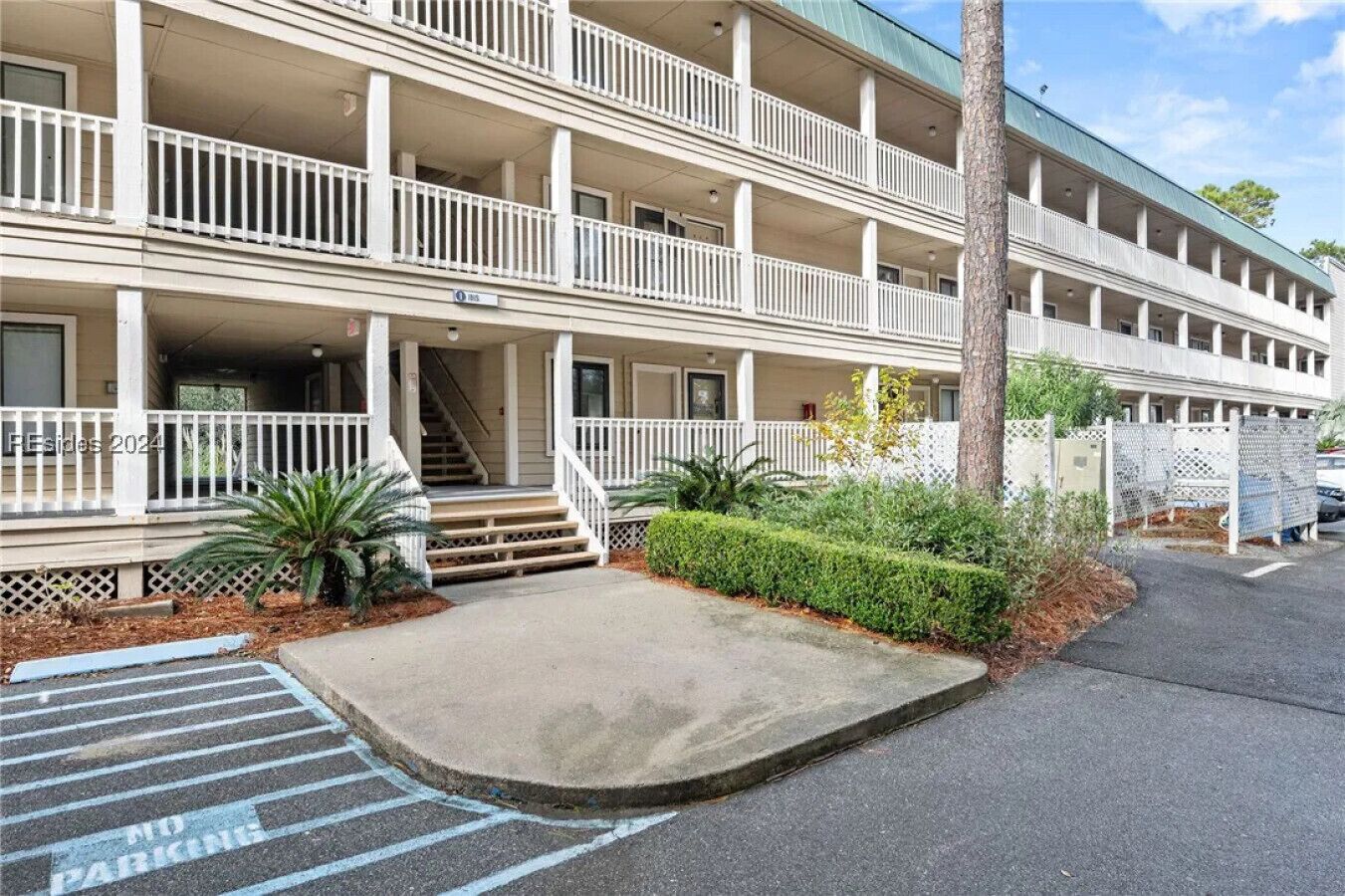 A multi-story building with a covered front porch, a parking area marked "No Parking," and a tree in the foreground.