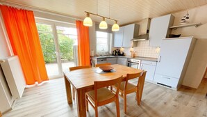 A kitchen with a dining table, chairs, a stove, oven, and a refrigerator. - Tannengrund - Comfortable vacation apartment little time out with terrace and garden (Loddin)