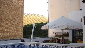 Un área de piscina con bordeado de azulejos, pared de ladrillo y un edificio con tejado estampado al fondo.