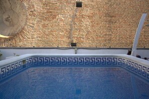 A swimming pool with a tiled edge and a brick wall in the background. - Joy Setas Coworking (Seville)