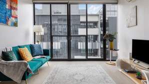 A modern living room with a teal sofa, a large window, and a flat-screen TV. - Luxury Living in Heart of South Yarra near Jam Factory, Prahran Market Chapel St (South Yarra)