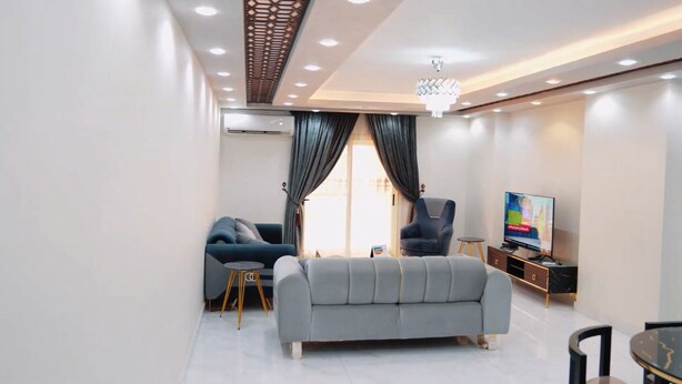 Una sala de estar moderna con un sofá gris, un sillón azul, una mesita redonda y un televisor sobre un mueble de madera.