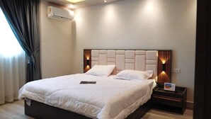 Habitación de hotel con una cama grande, una mesita de noche con lámpara y un equipo de aire acondicionado en la pared.