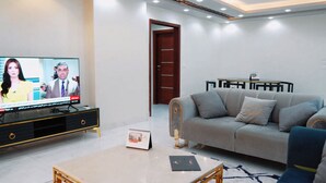 Una sala moderna con televisión de pantalla plana, un sofá, una mesa de centro y un comedor con una pequeña mesa y sillas.