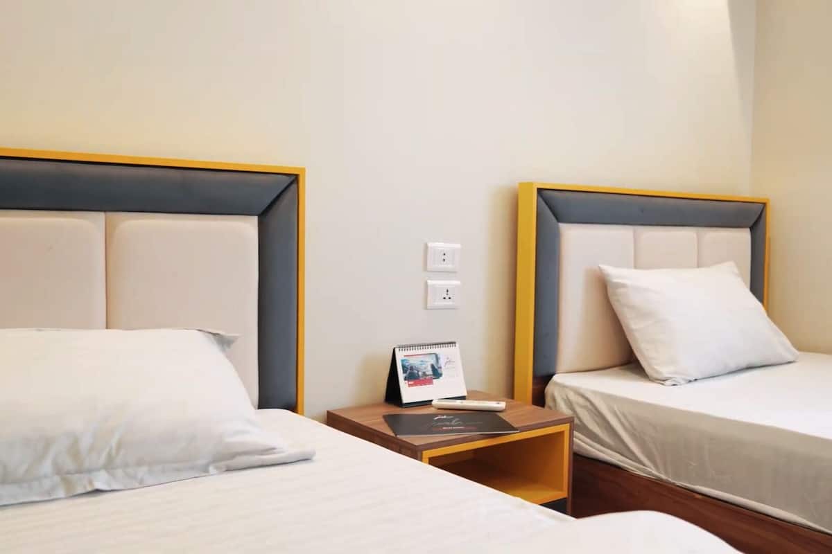 A hotel room with two beds, each with a headboard and white bedding. There is a nightstand between the beds with a book and a small table lamp.