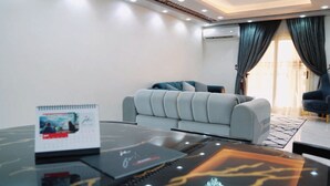 Una sala moderna con un sofá gris, una mesa de centro negra y un sillón azul.