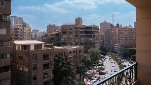 Un paisaje urbano con varios edificios altos, una calle concurrida con coches y un cielo despejado.