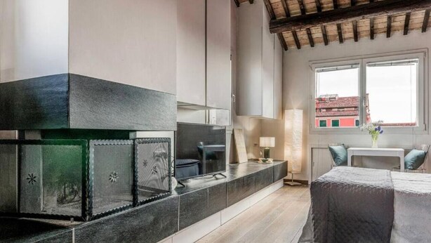A modern kitchen with a built-in stove, a dining area with a table and chairs, and a view of the city through a window. - enJoy Home - Attic Room in Lords' Square (Padova)