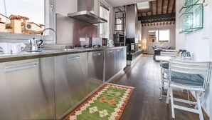 A modern kitchen with stainless steel appliances, a central island, and a dining area with white chairs. - enJoy Home - Attic Room in Lords' Square (Padova)