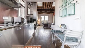 A modern kitchen with stainless steel appliances, a dining area with white chairs, and a staircase leading to an upper level. - enJoy Home - Attic Room in Lords' Square (Padova)