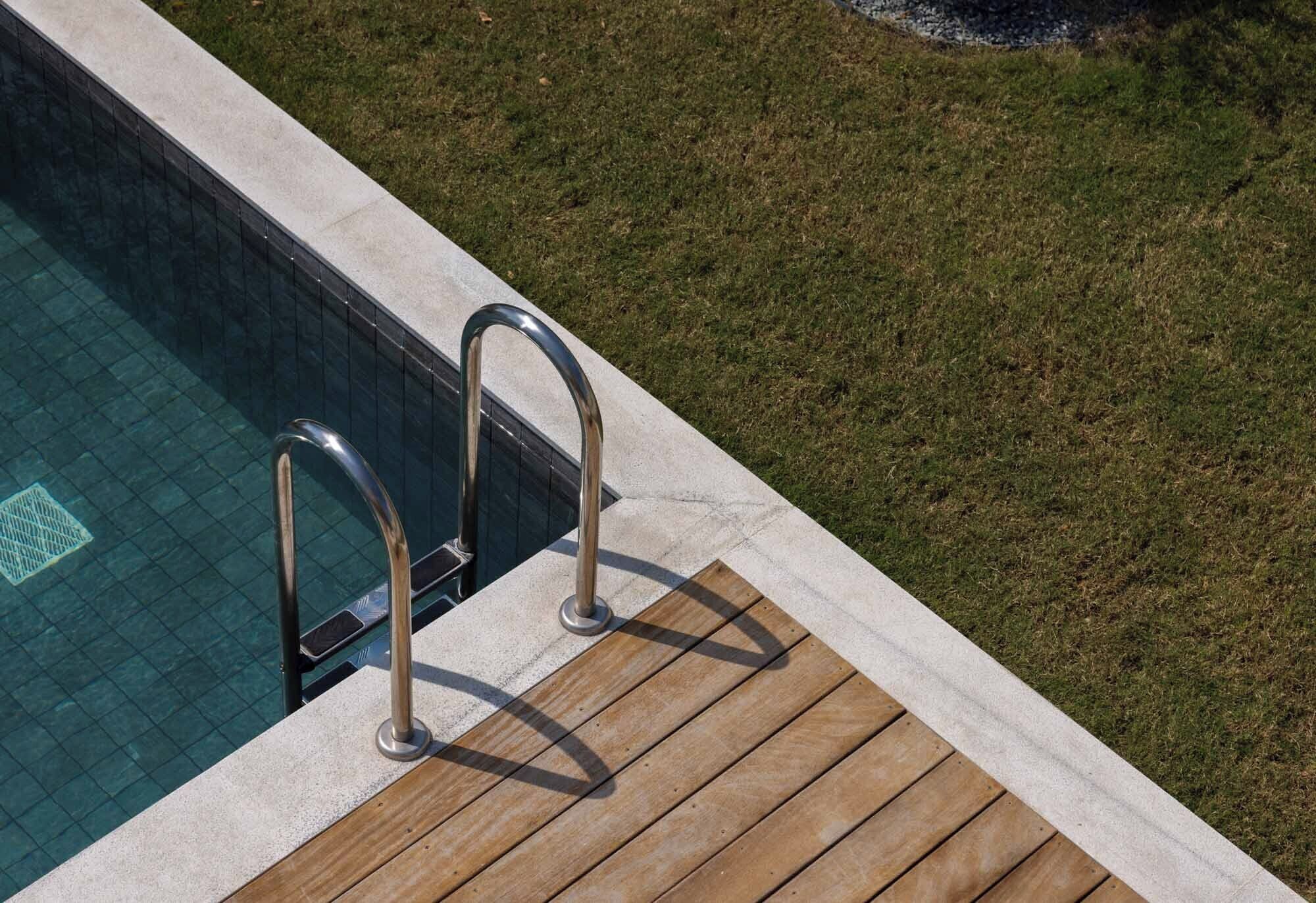 A swimming pool with a wooden deck and metal handrails.