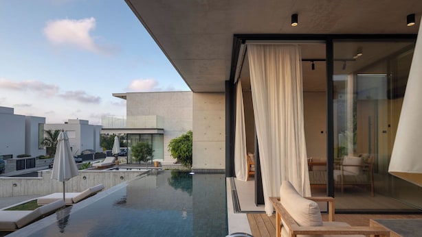 A modern infinity pool with a glass balustrade, lounge chairs, and a view of a cityscape.