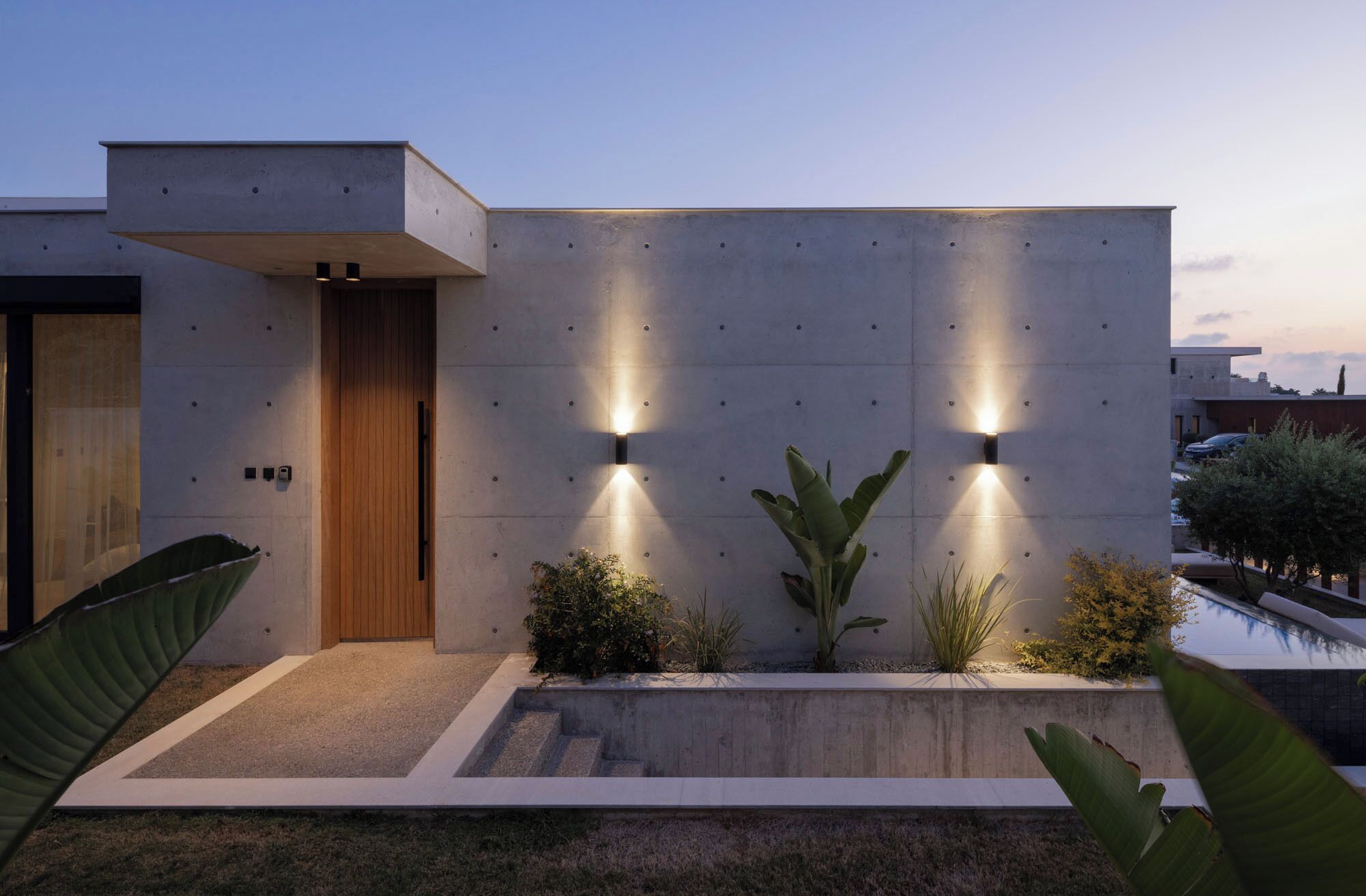 A modern building with a concrete facade, a wooden door, and two wall-mounted lights.