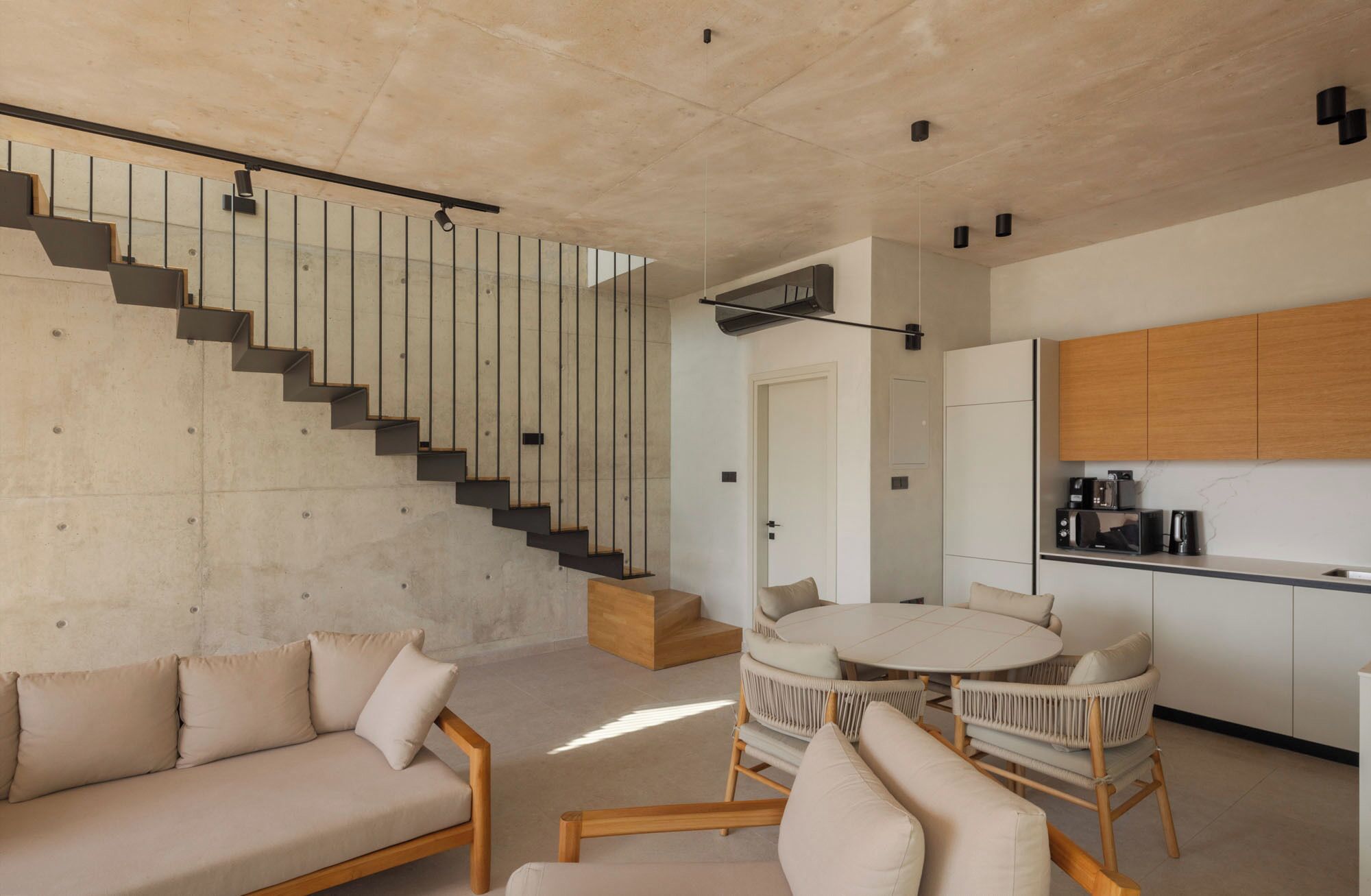 A modern living room with a staircase, a dining area, and a kitchen.