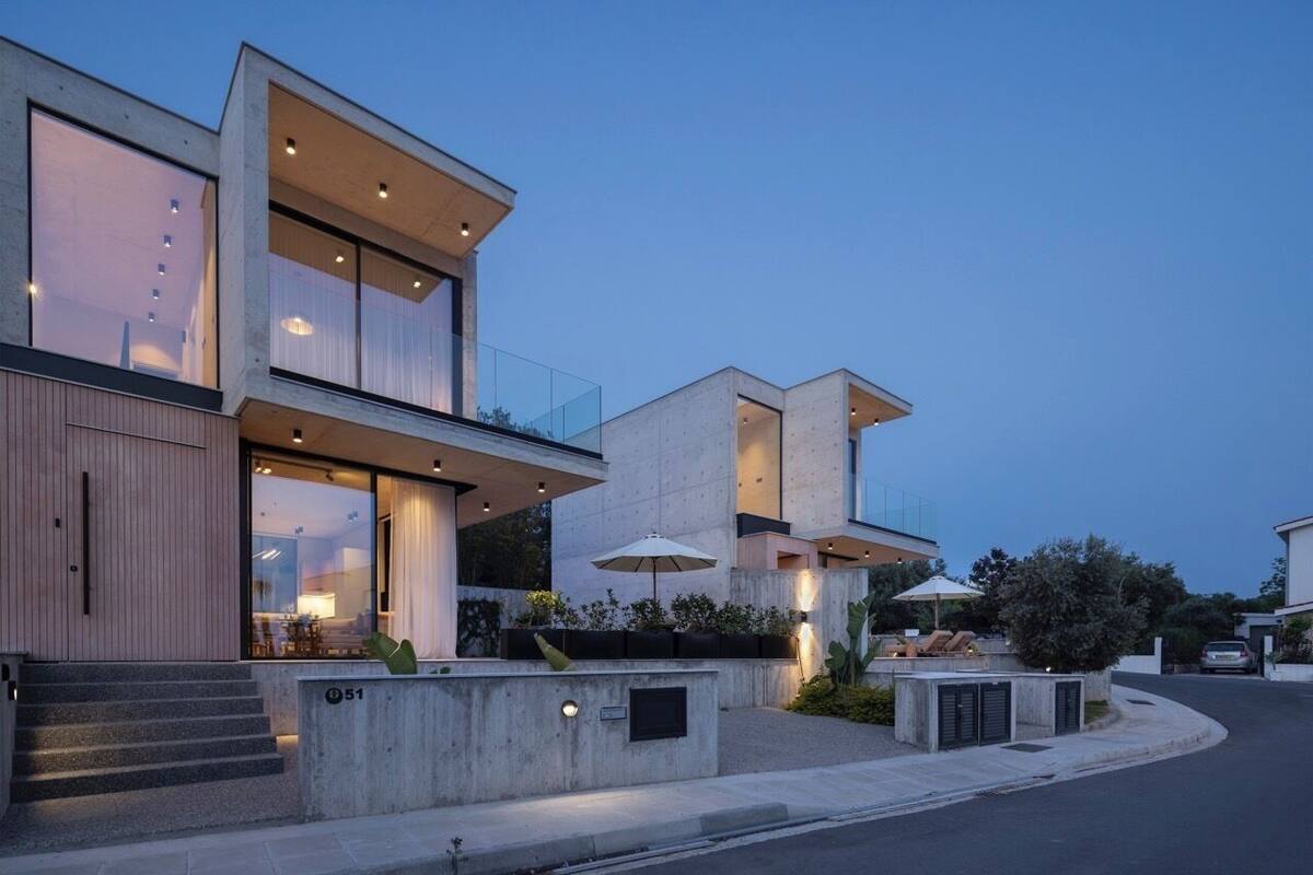 A modern two-story house with large windows, a concrete exterior, and a small outdoor seating area with umbrellas.