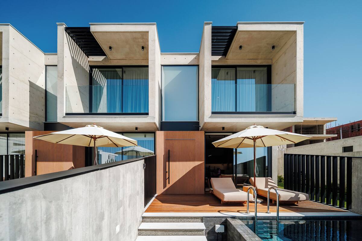A modern multi-story building with a swimming pool, outdoor seating, and large umbrellas.
