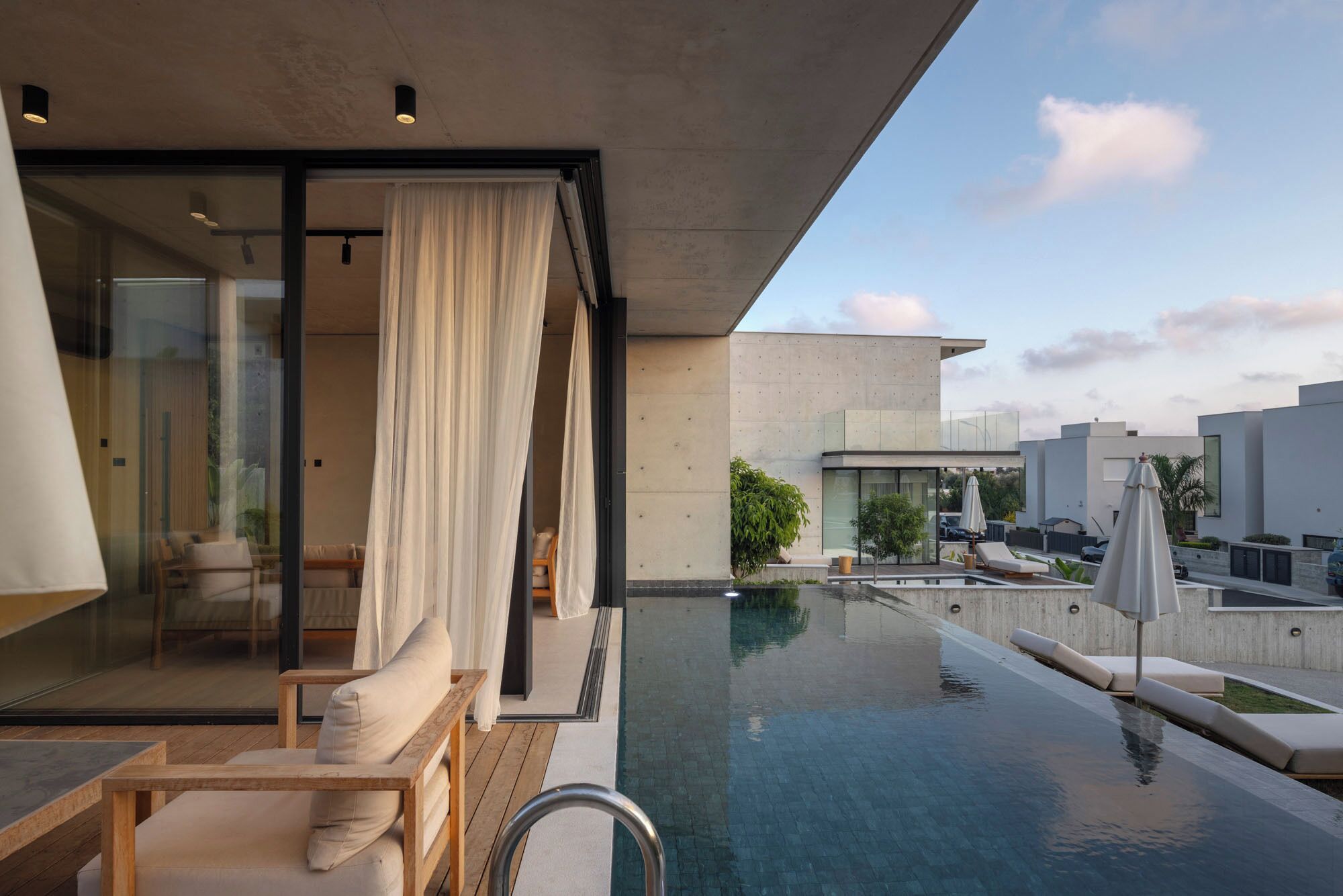 A modern outdoor pool area with a glass-enclosed lounge, white curtains, and a view of the surrounding buildings.