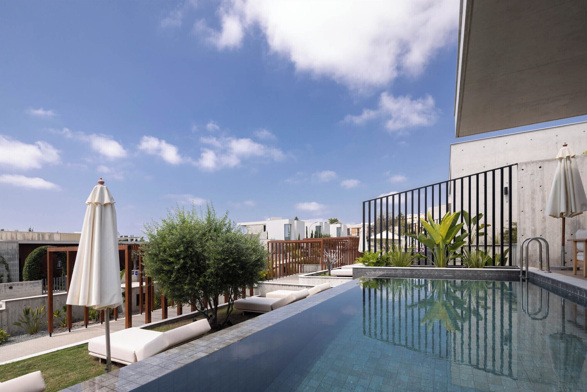 A modern outdoor pool area with a clear blue sky, a white umbrella, and a metal fence.