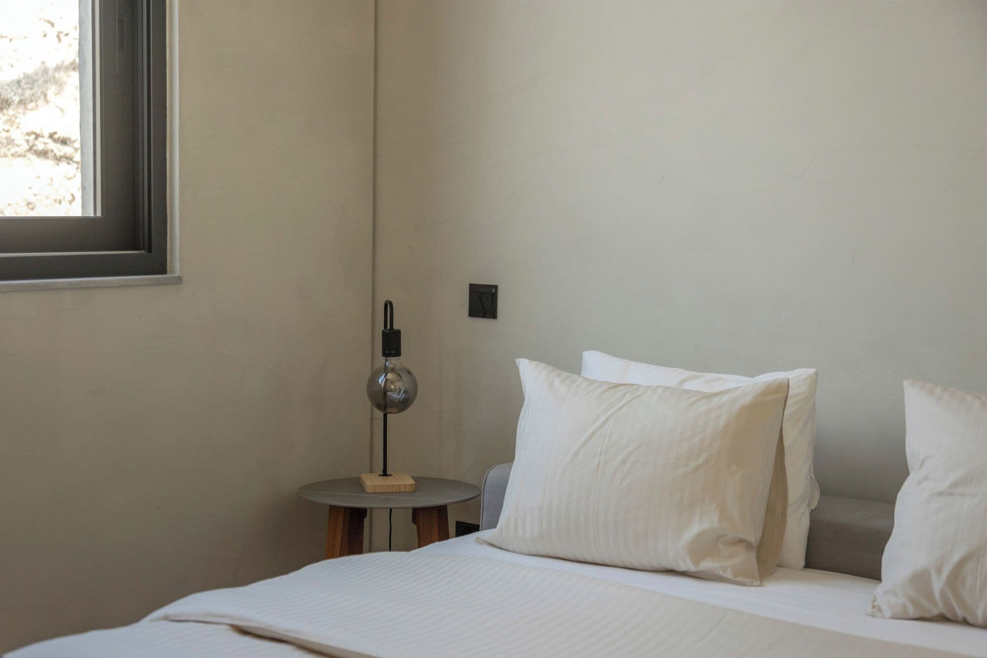 Une chambre à coucher avec un lit, des oreillers, une table de chevet, une lampe et une fenêtre.
