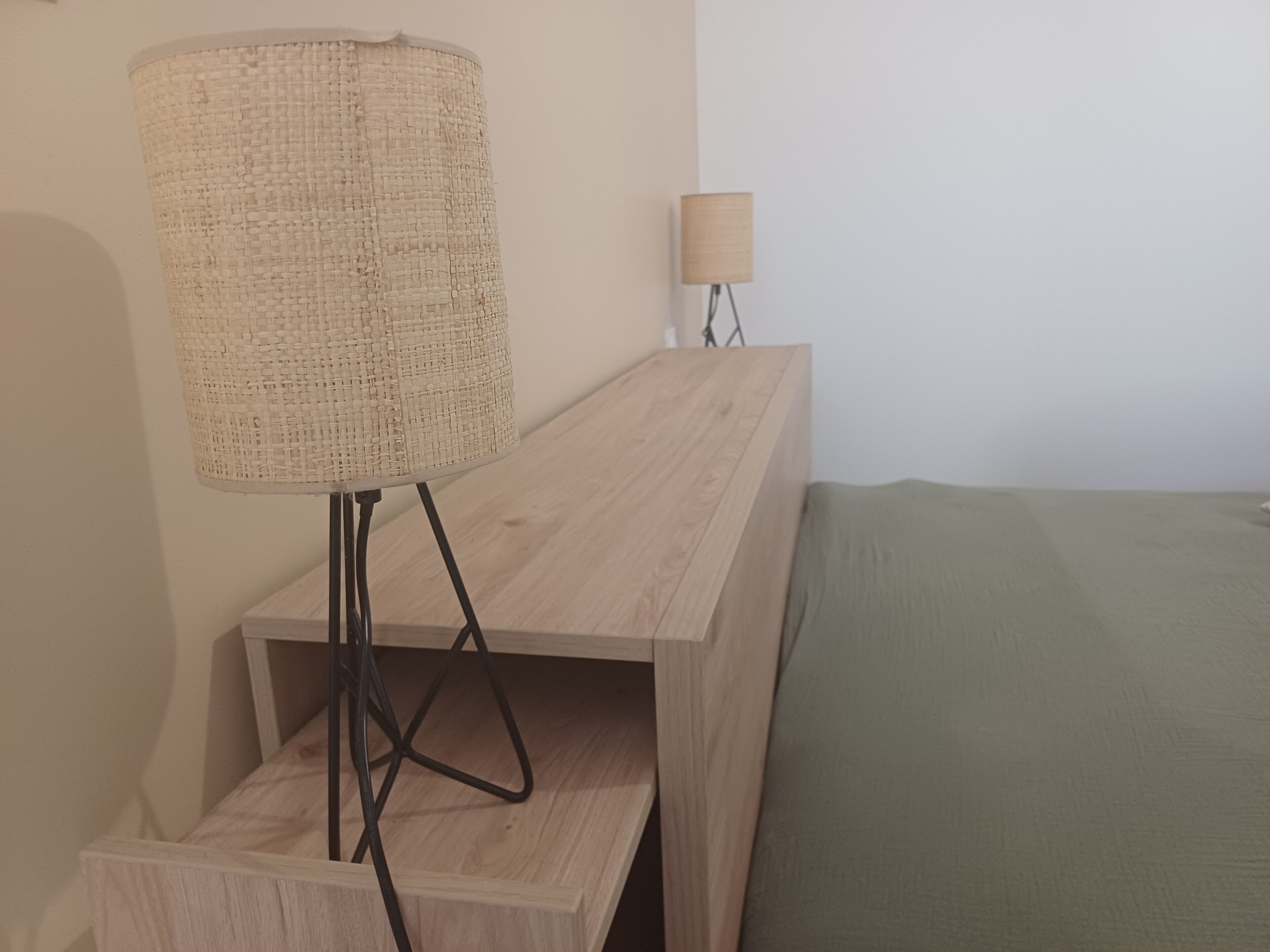 Et værelse med et træskrivebord, en vævet lampe og en grøn seng.