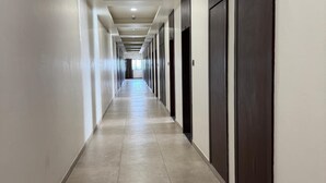 A long, narrow hallway with a tiled floor and a series of doors on one side. - TGR Hotel (Mundra)