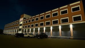 A multi-story hotel with a row of parking spaces in front. - TGR Hotel (Mundra)