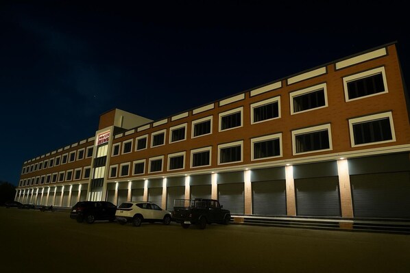 A multi-story hotel with a row of parking spaces in front. - TGR Hotel (Mundra)