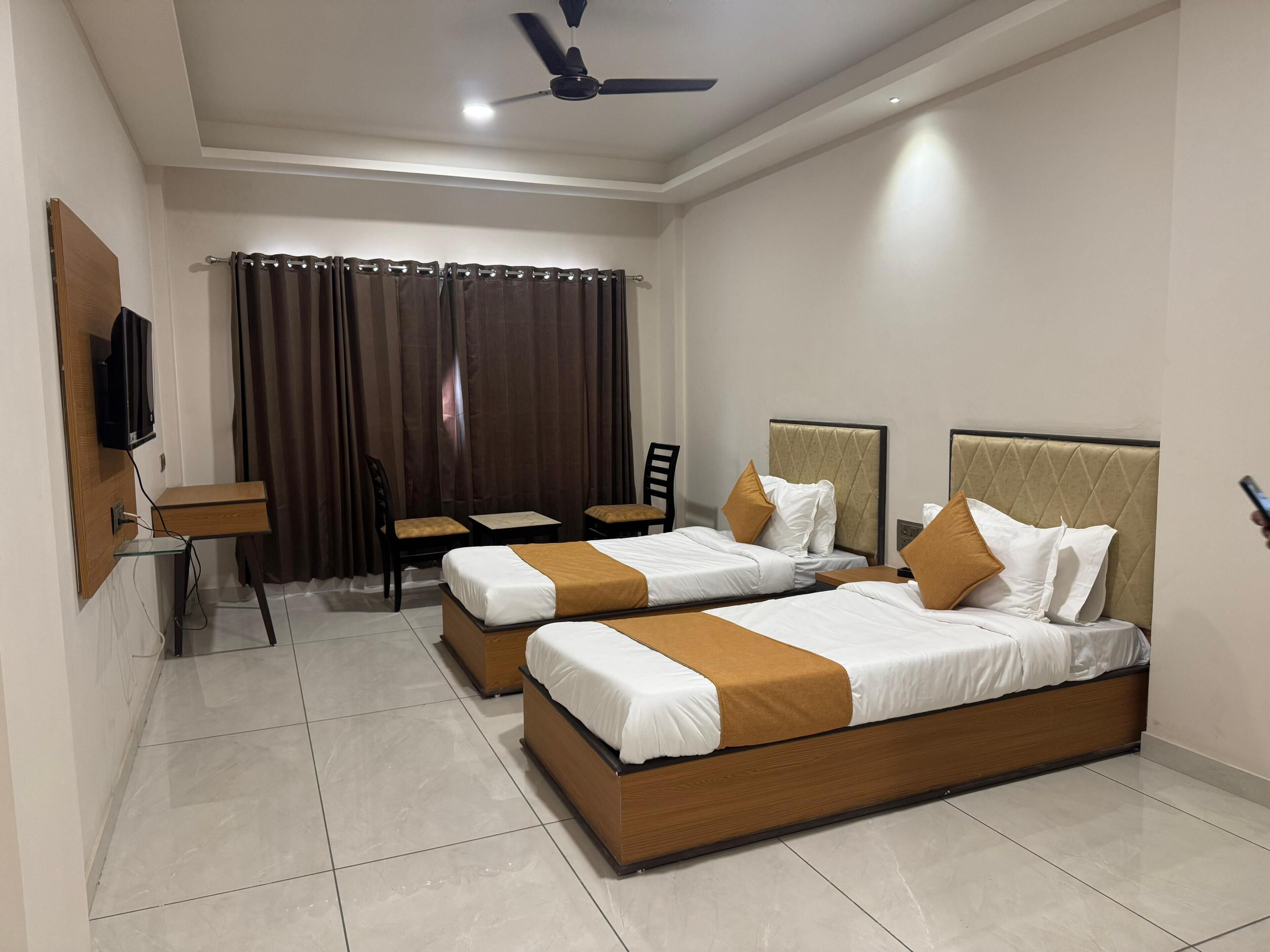 A hotel room with two beds, a desk, a chair, and a TV.