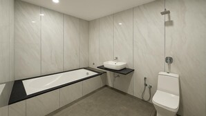 A modern bathroom with a rectangular bathtub, a pedestal sink, and a toilet. - TGR Hotel (Mundra)