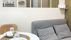 A modern room with a round dining table set for two, a grey sofa, and a large mirror on the wall.