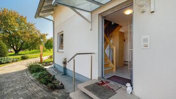 Ein Gebäudeeingang mit Glastür, einer Holztreppe im Inneren und einer kleinen Hundestatue vor der Tür.