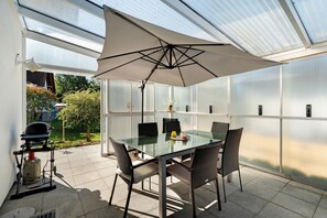 A glass-top table with four chairs, an umbrella, and a grill outside a building with a view of greenery. - Holiday Home 'Langer' with Mountain View, Private Terrace and Wi-Fi (Oberkirch)