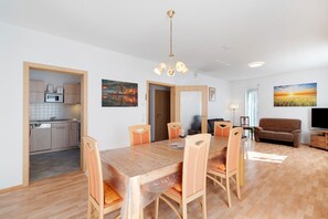 A modern living space with a wooden dining table, chairs, a kitchen area, a sofa, and a TV. - Holiday Home 'Langer' with Mountain View, Private Terrace and Wi-Fi (Oberkirch)