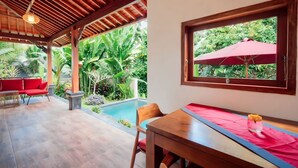 A covered outdoor area with a pool, red seating, and lush greenery visible through a window. - Soma Uma Dhara private pool villa designed for soulful rest and natural luxury. (Bali)