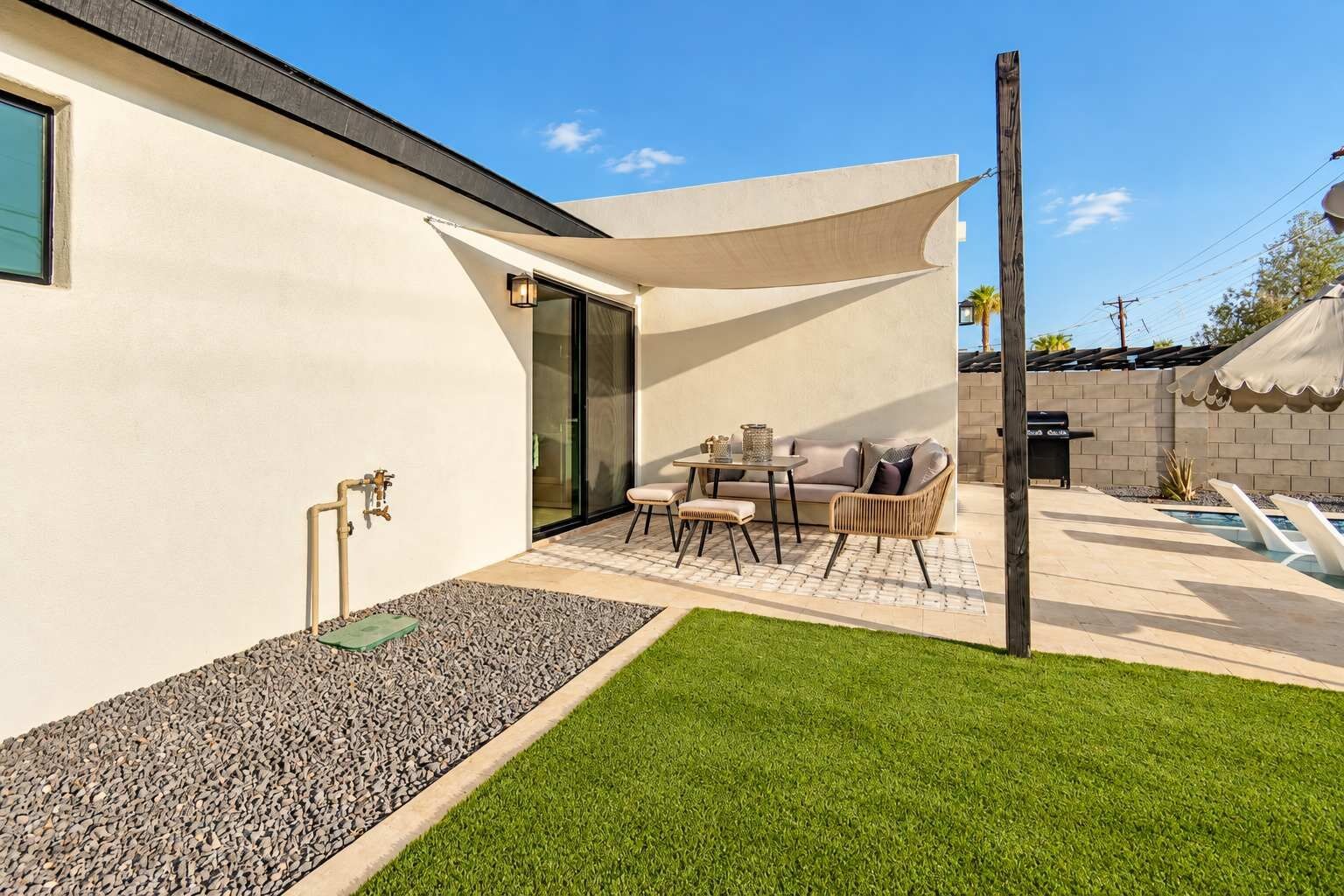 A modern outdoor patio with a table and chairs, a barbecue grill, and a swimming pool.