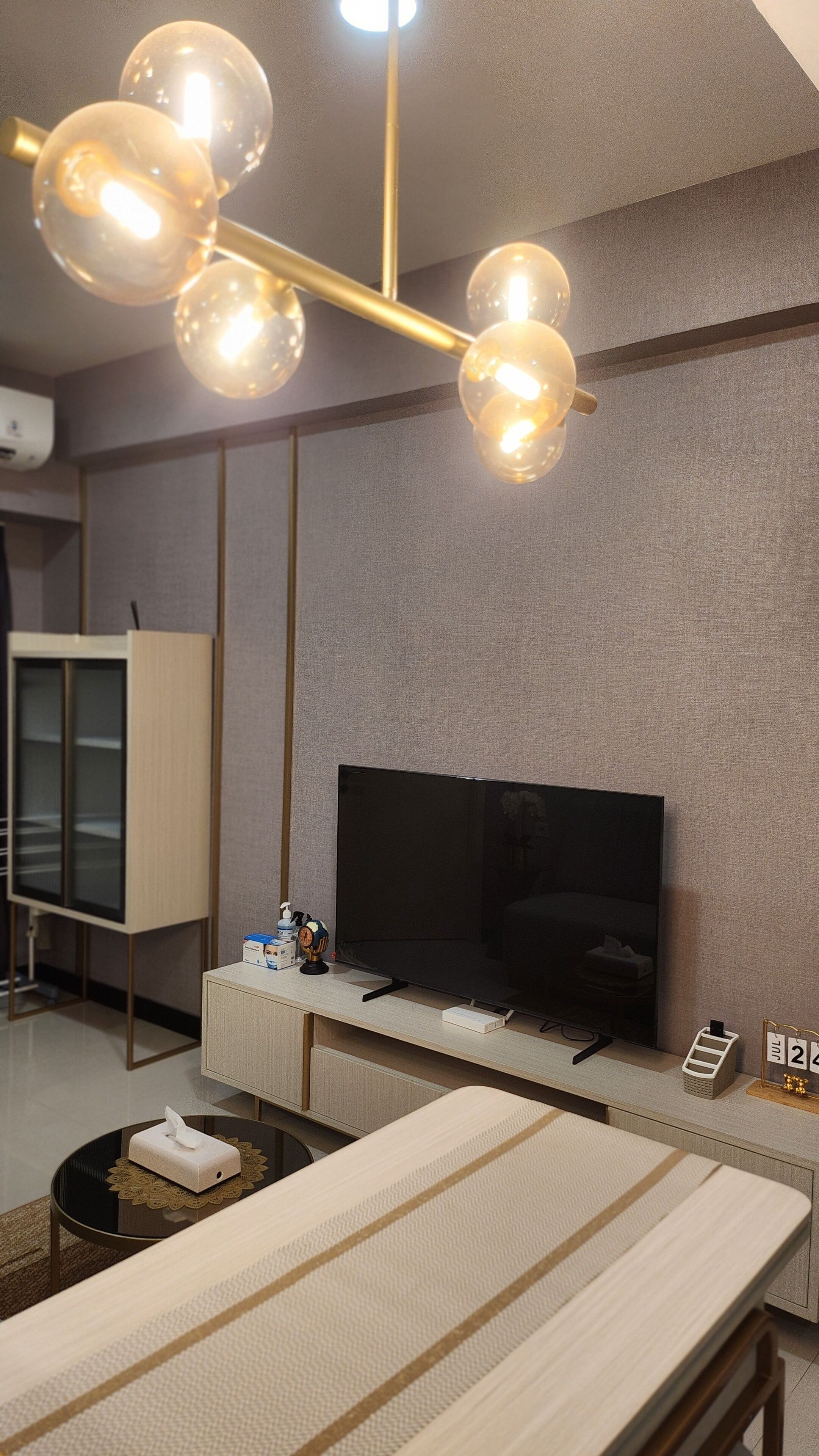 A modern living room with a flat-screen TV, a wooden cabinet, a glass-top coffee table, and a unique spherical chandelier.