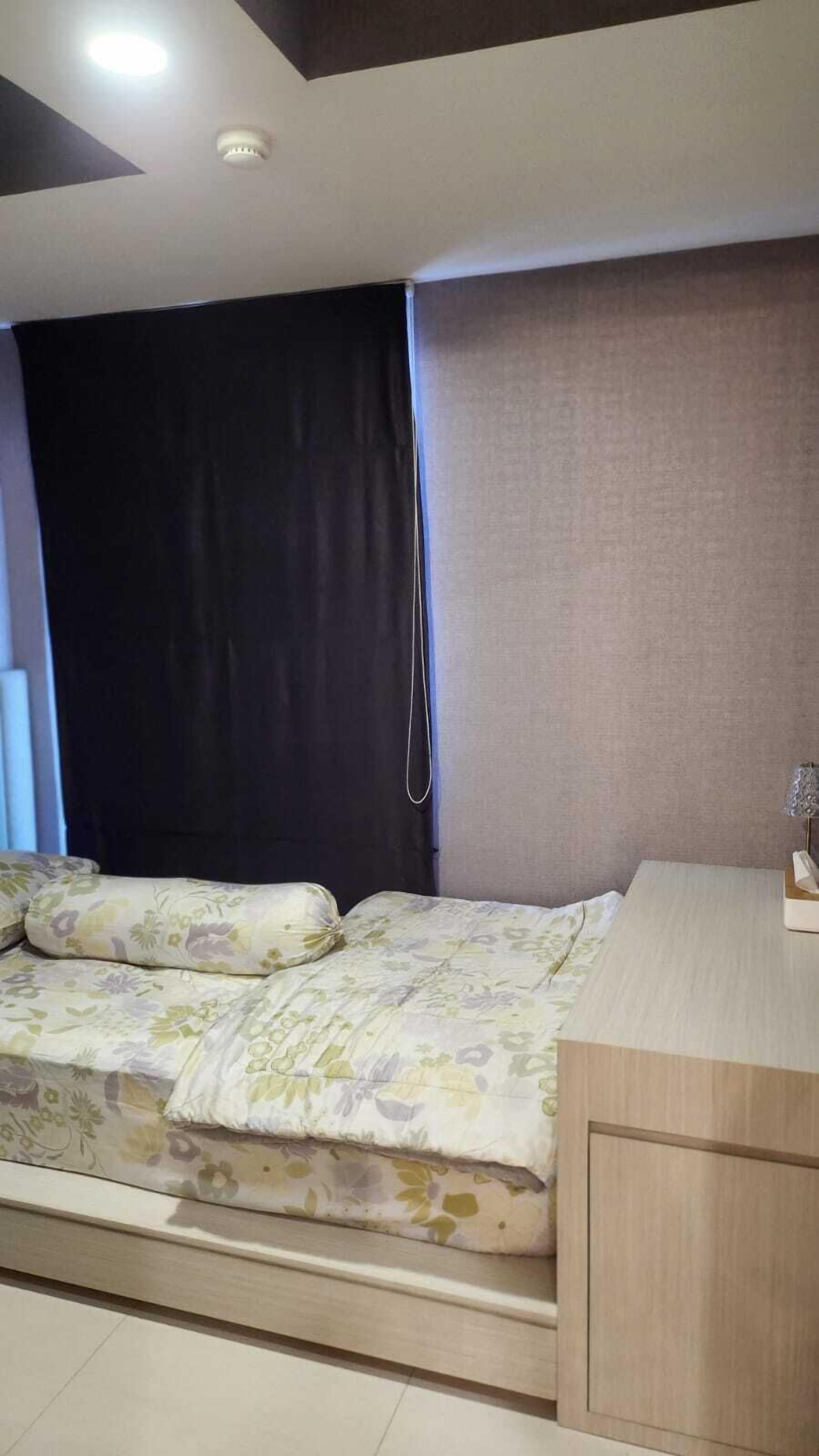 A bedroom with a bed, a desk, a curtain, and a ceiling light.