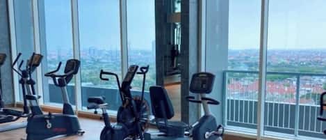 Un gimnasio con máquinas de cardio y amplias ventanas que ofrecen vista a la ciudad.