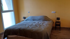 Un dormitorio con cama, dos mesitas de noche, una ventana y un enchufe.