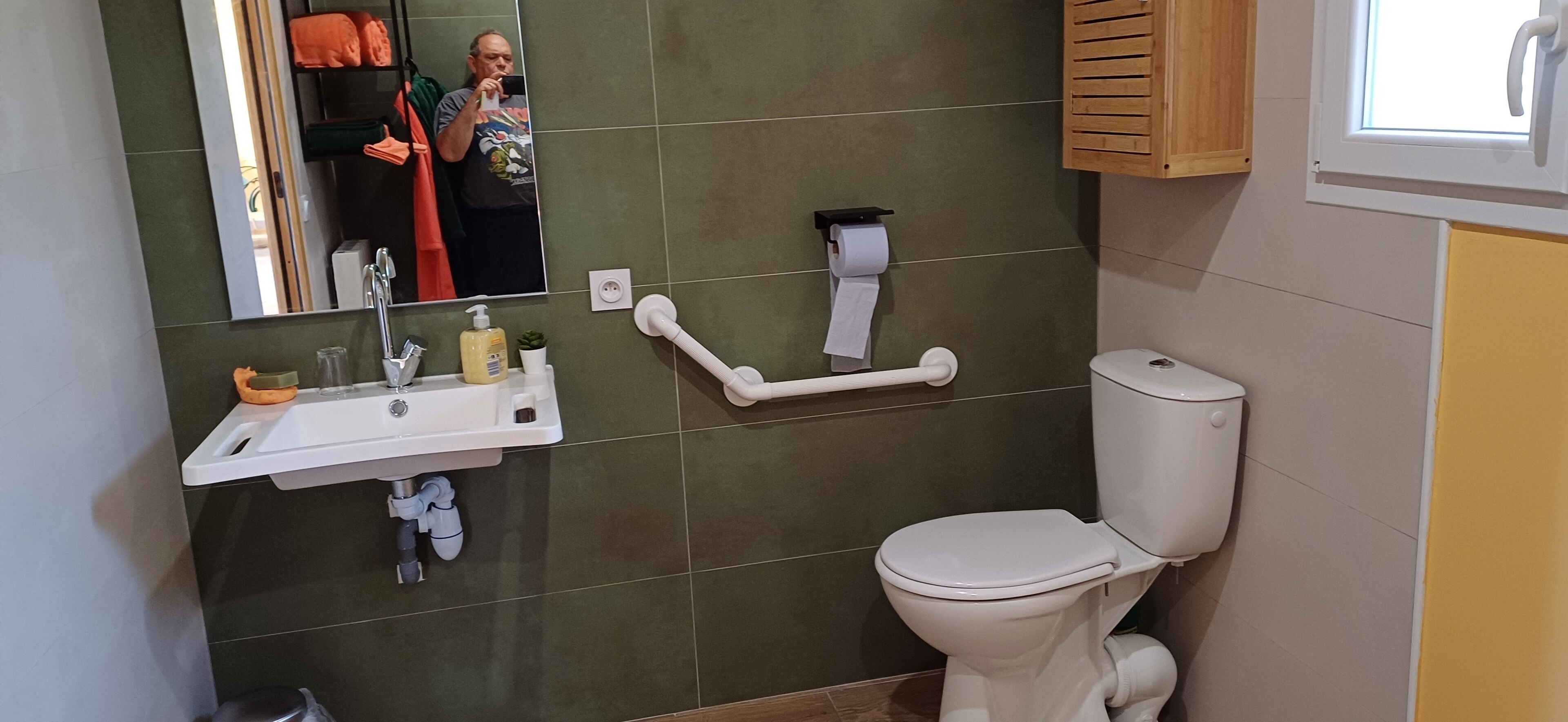 Un baño con un lavabo blanco, paredes con azulejos verdes, un inodoro blanco y un espejo.