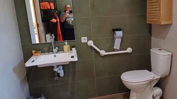 Un baño con un lavabo blanco, paredes con azulejos verdes, un inodoro blanco y un espejo.