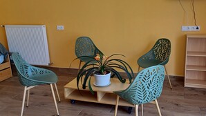 Una habitación con una pared amarilla, un radiador, una mesa de madera con sillas, una planta en maceta y una estantería de madera.