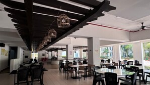 Un vaste espace intérieur aménagé en salle à manger, avec de nombreuses tables et chaises, un bar central et de grandes fenêtres offrant une vue sur l’extérieur.