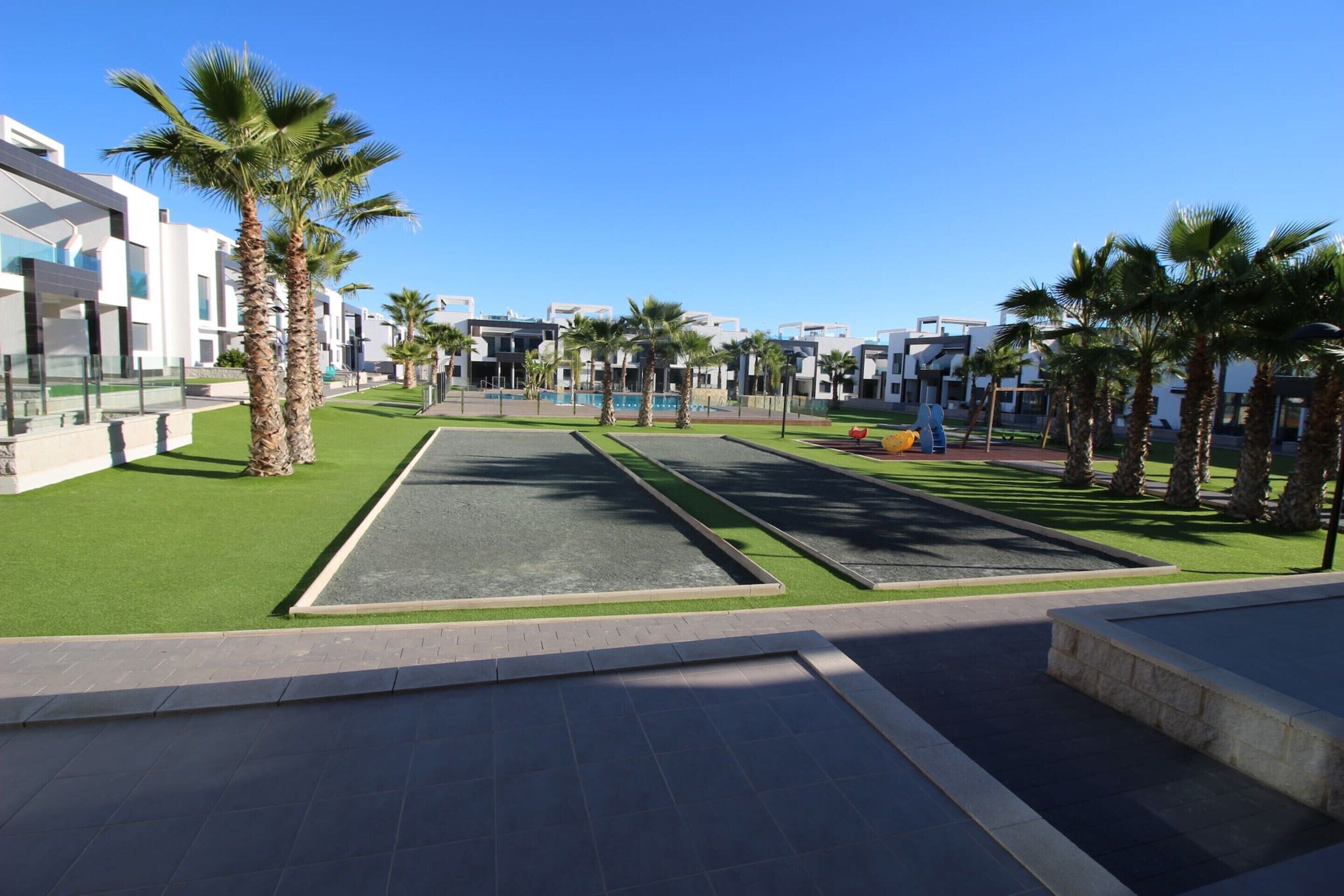 A modern outdoor area with palm trees, a green lawn, and a paved walkway.