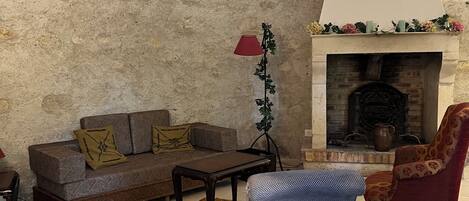 Una sala de estar con pared de piedra, chimenea, sofá, sillón y alfombra estampada.