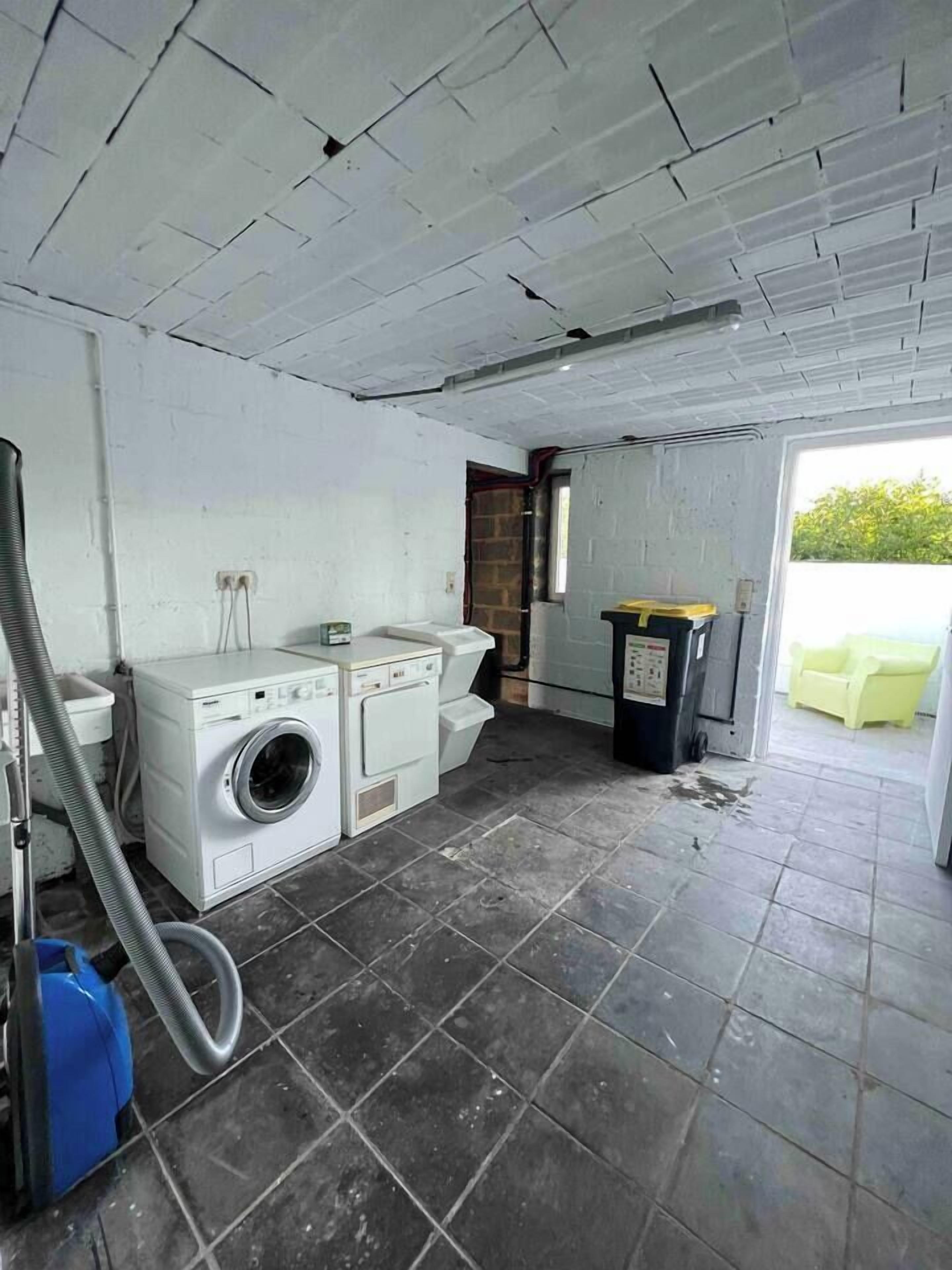 A laundry room with a washing machine, dryer, and a trash bin.