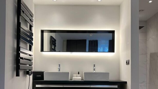 Une salle de bain moderne avec un grand miroir, deux lavabos et un meuble-lavabo noir.