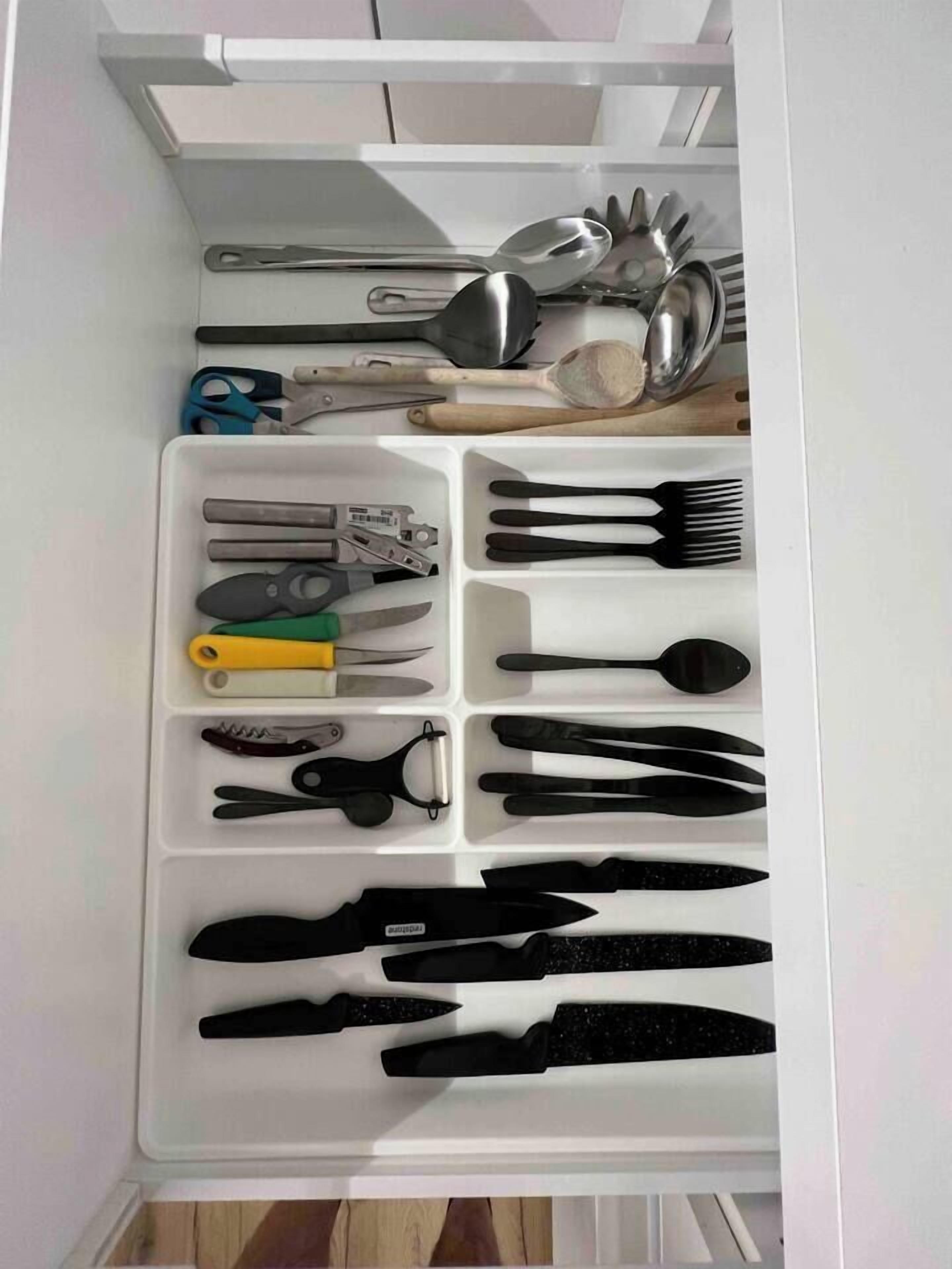 Un cajón con diversos utensilios y herramientas de cocina, incluyendo tijeras, cuchillos y una cuchara.