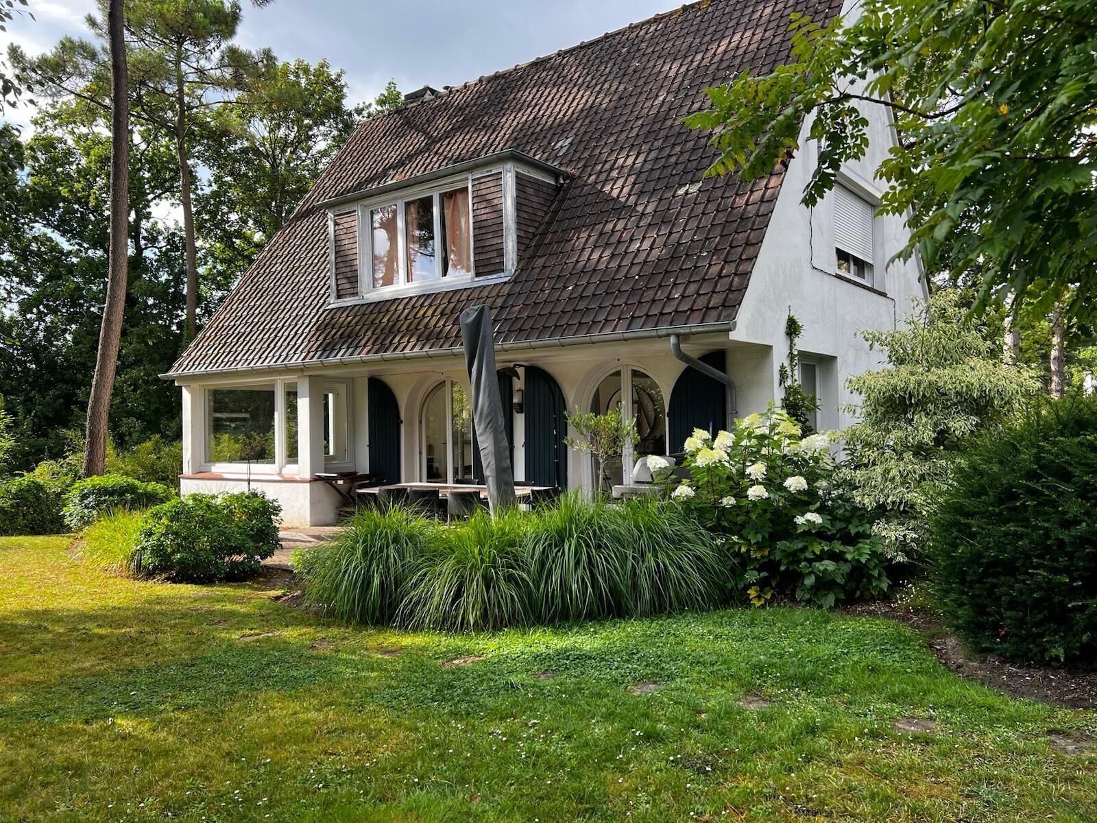 Une maison à deux étages, avec un toit en tuiles, une véranda et un jardin bien entretenu.